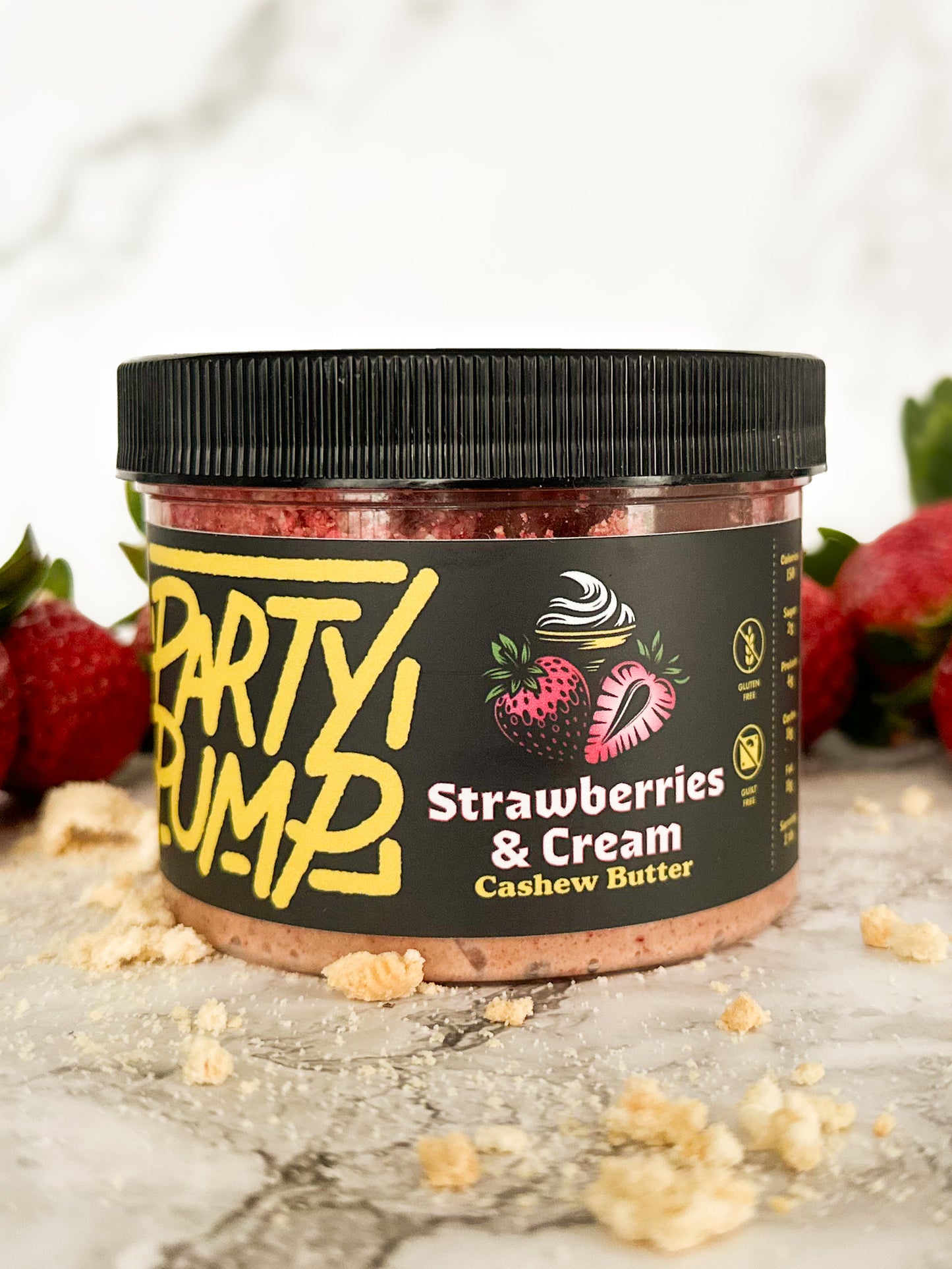 Image of a closed jar of the Strawberries and Cream flavored cashew nut butter spread with cookie crumbs in the foreground and strawberries in the background.