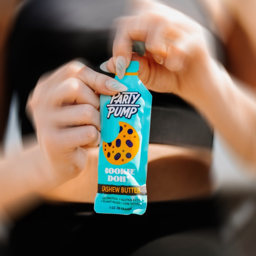 Hand holding a 'Party Pump' cookie dough cashew butter packet