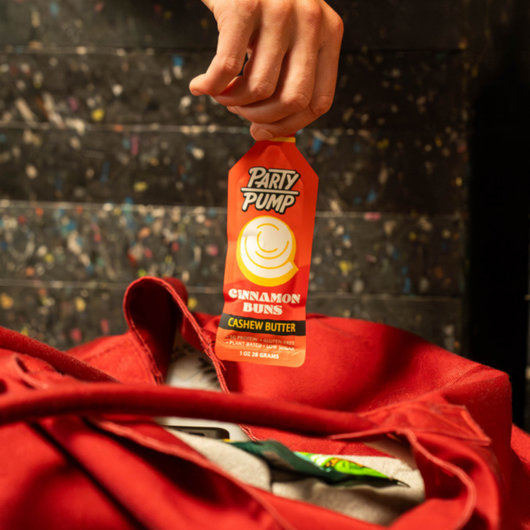 Party Pump Cinnamon Buns Squeezie – hand holding a cinnamon buns Squeezie over a red bag with a colorful background