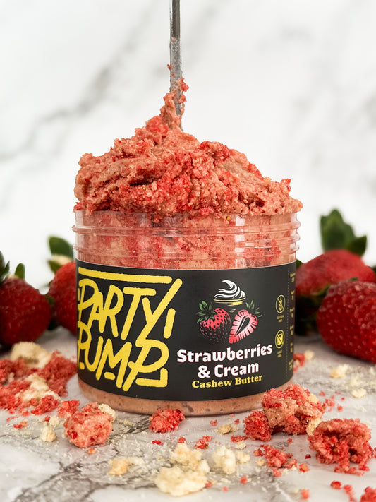 Close up image of the texture of the Strawberries and Cream flavored cashew nut butter spread alongside crumbs and strawberries. 